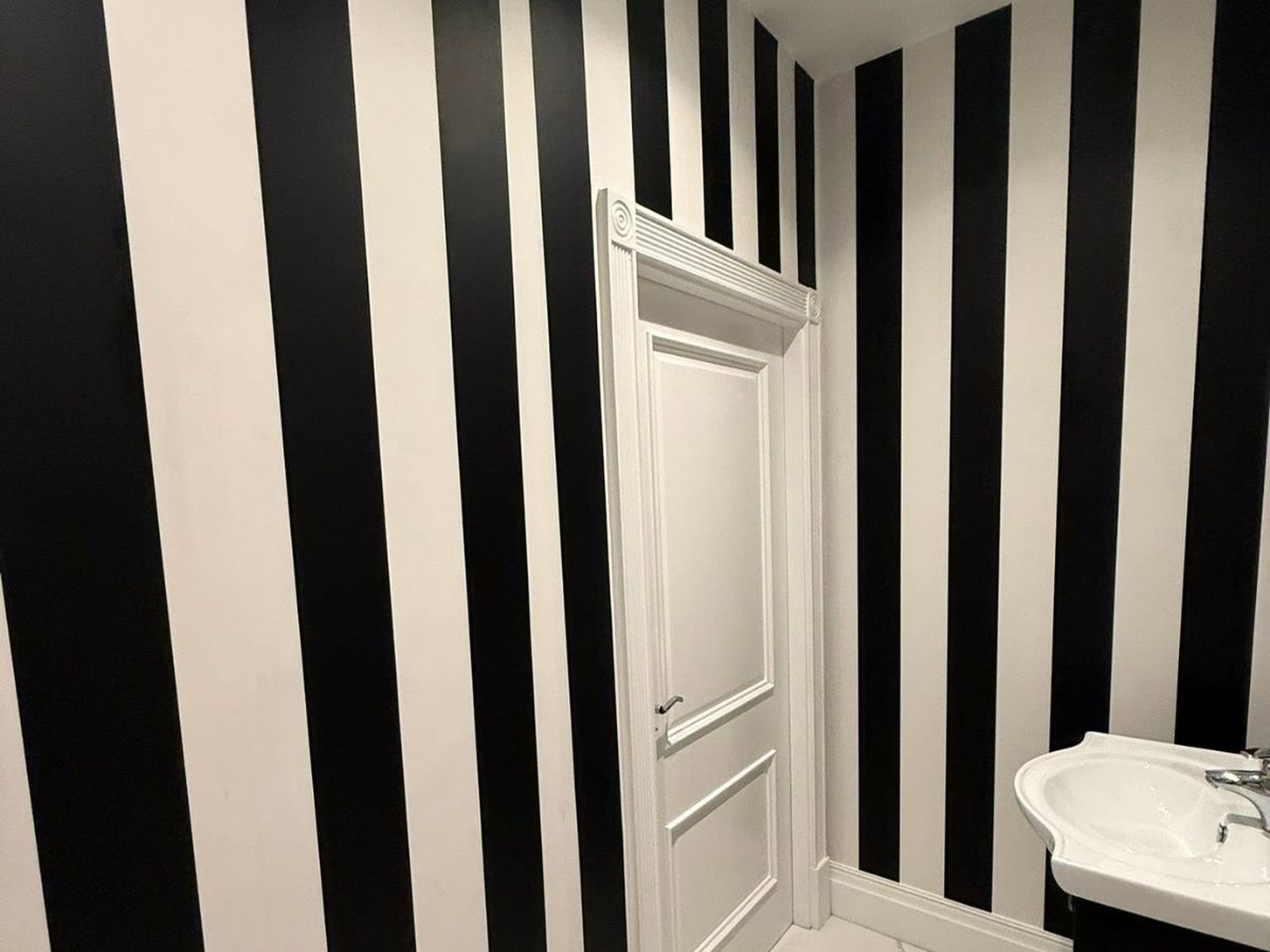 Bold black and white vertical striped wallpaper installed around an interior doorway and bathroom fittings.