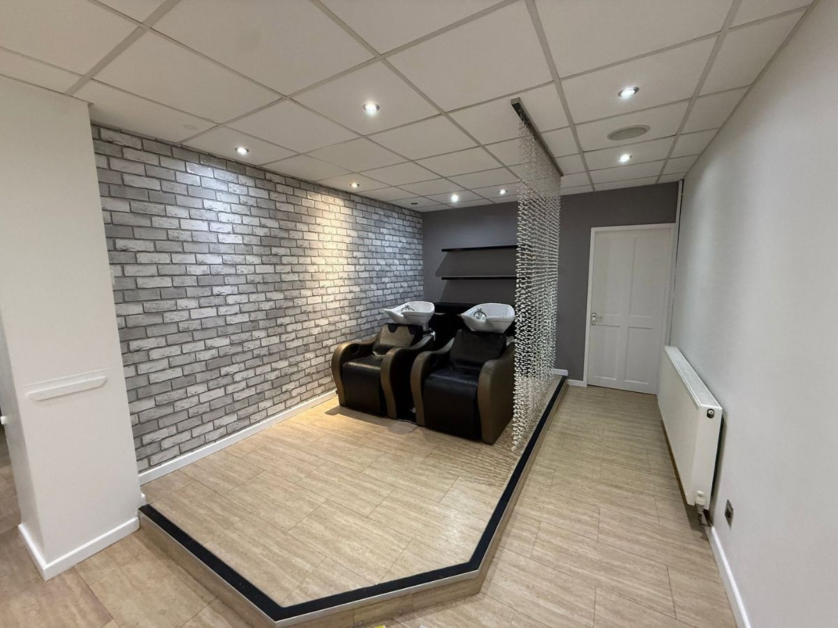 Hair salon wash area featuring decorative brick-effect wallpaper, grey painted walls and contemporary flooring.