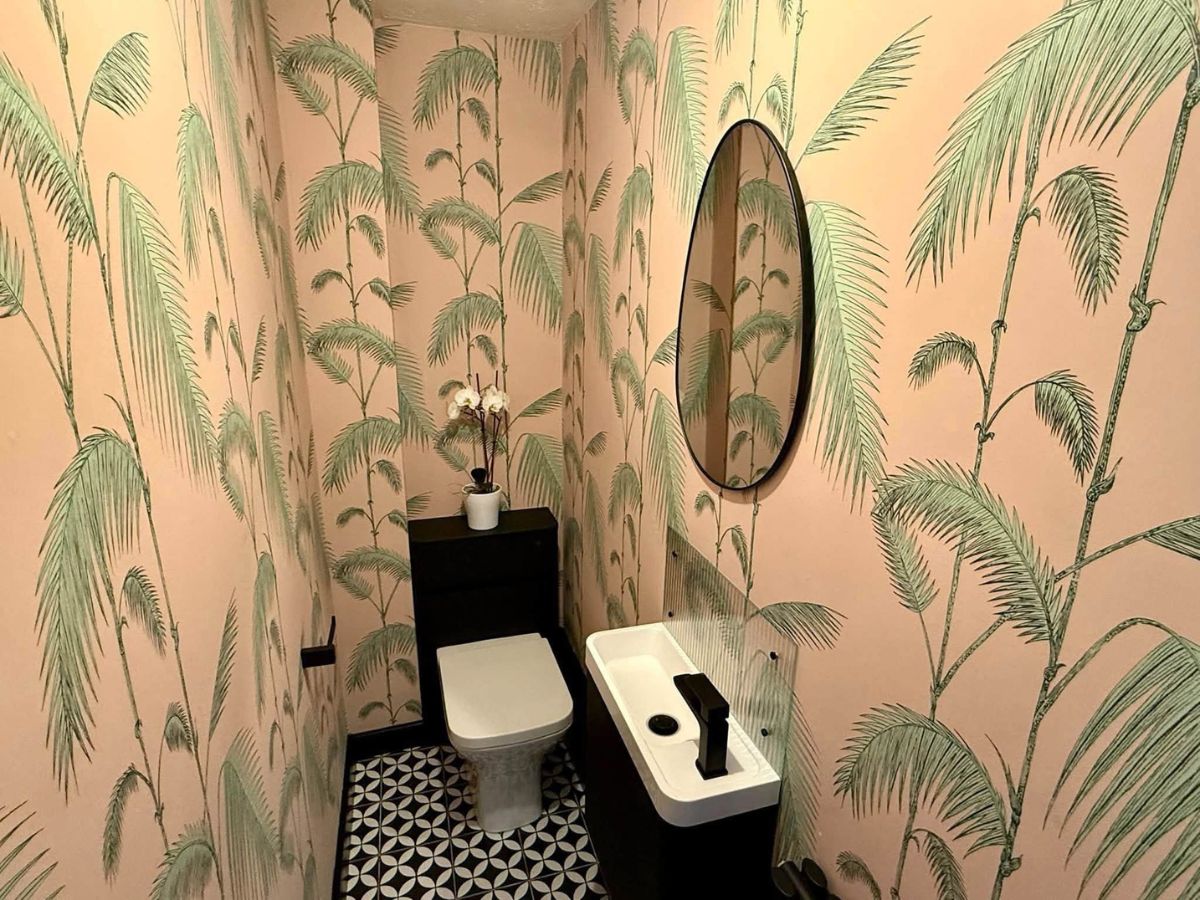 Cloakroom decorated with tropical palm leaf wallpaper, contrasting black fittings and patterned floor tiles.
