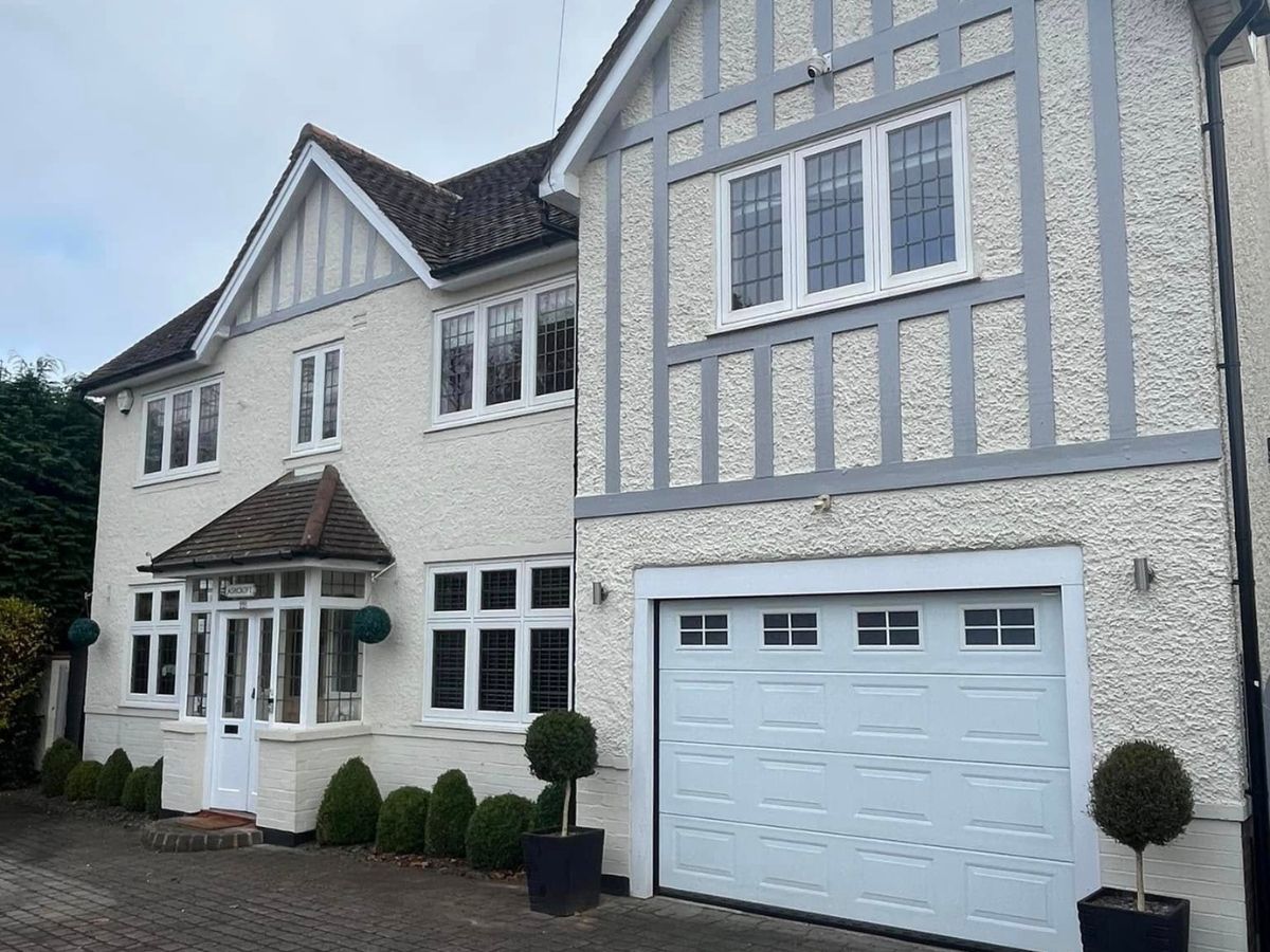 Exterior of a residential property featuring white rendered walls, grey decorative timber detailing and white painted windows.