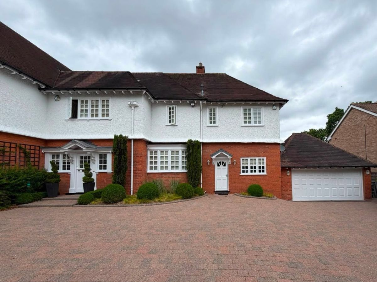 Large residential property with white painted exterior walls, red brickwork and a matching detached garage.