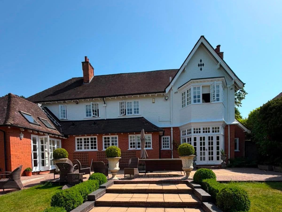 Exterior of a large residential property featuring white painted walls, red brickwork and landscaped gardens.