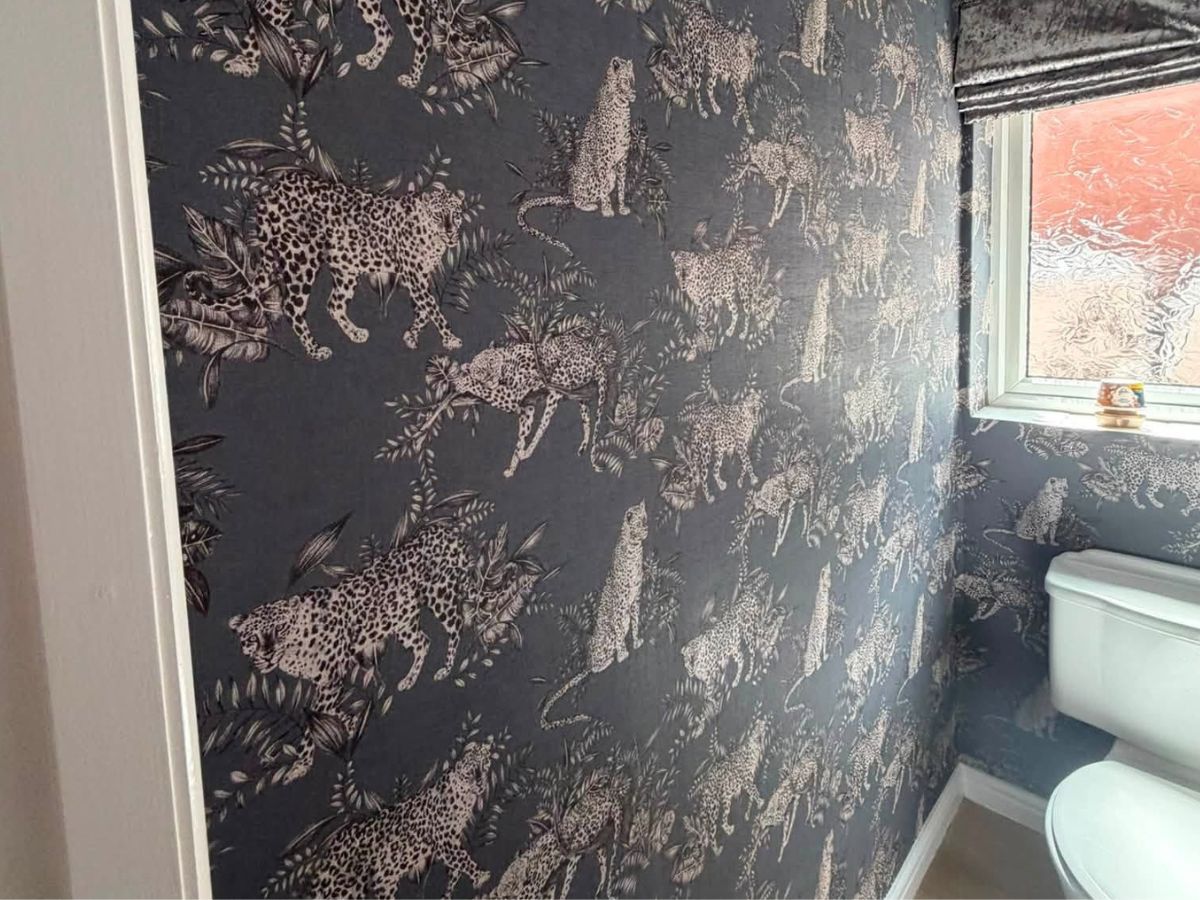 Dark leopard-patterned feature wallpaper professionally fitted around a bathroom window and sanitary fittings.