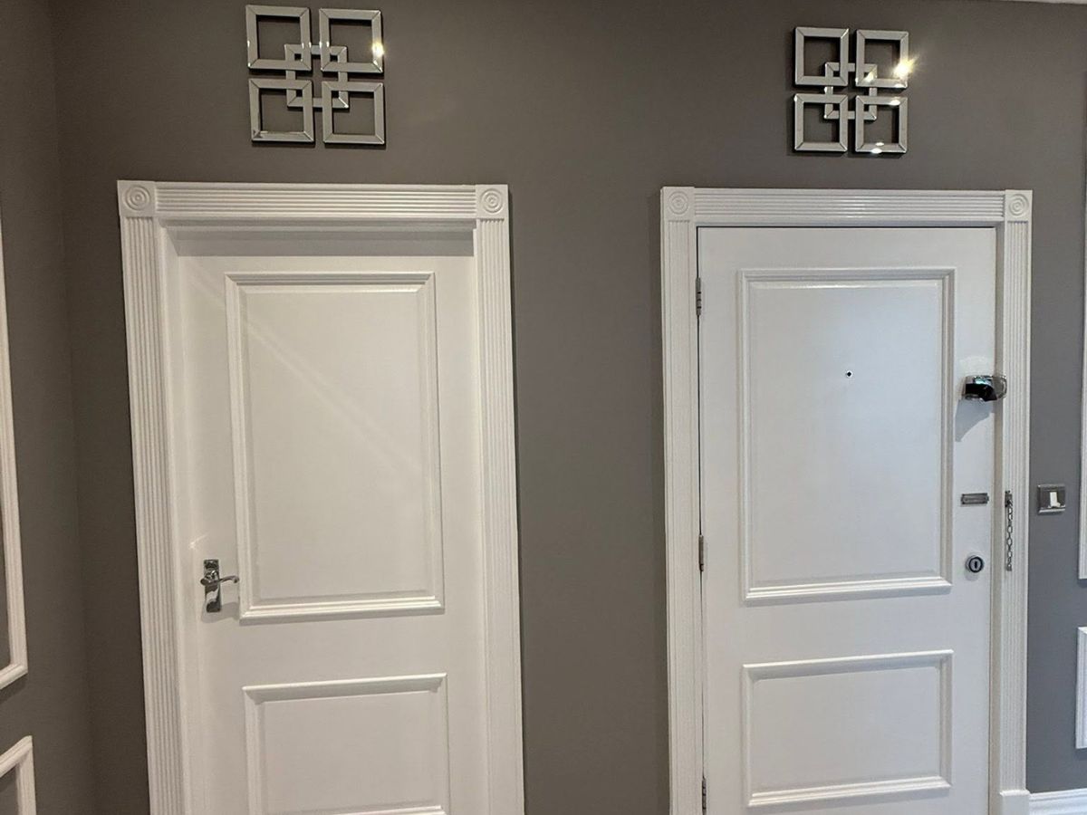 Two white painted panelled interior doors with decorative architraves against a contrasting grey painted wall.