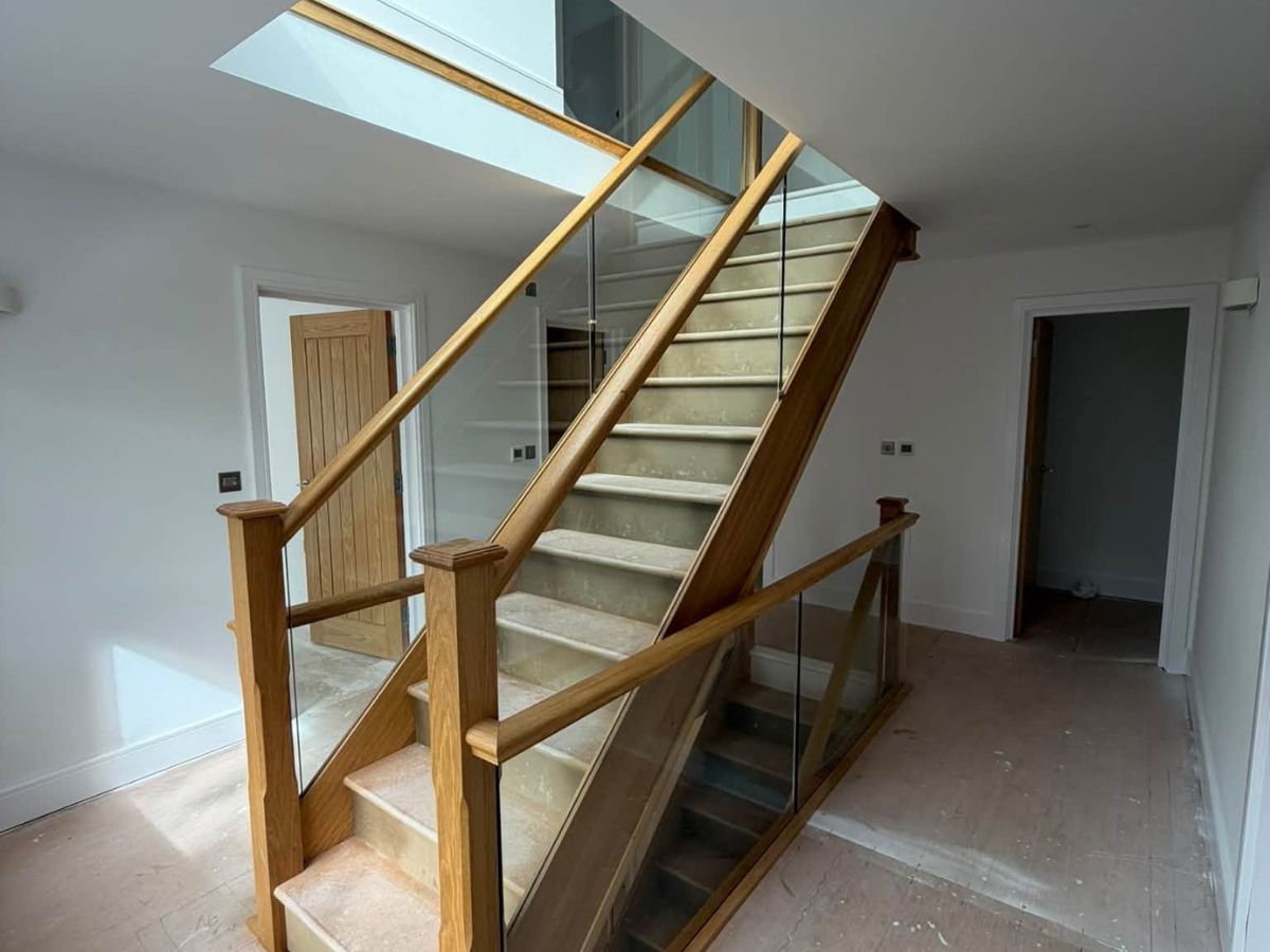 Modern staircase with natural wood handrails, glass balustrades and freshly painted white surrounding walls.