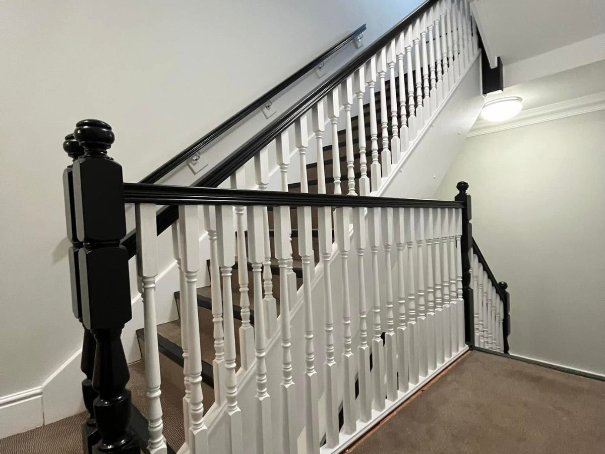 Traditional staircase featuring black painted handrails and newel posts with contrasting white balustrades and walls.